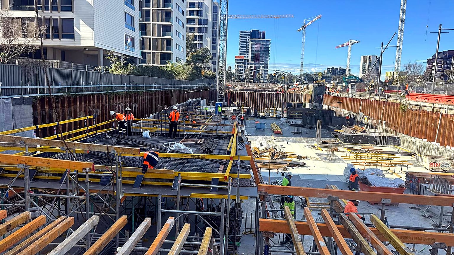 Site crew installing reinforcement and slab formwork in a deep urban excavation.