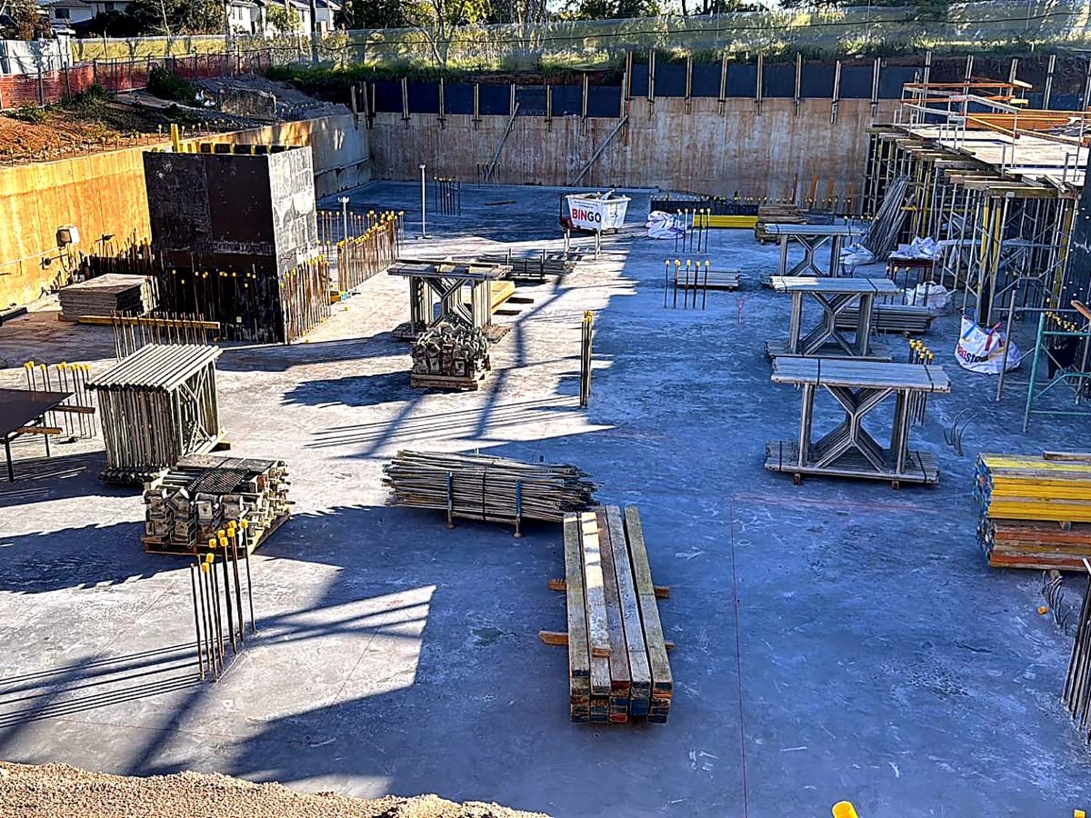Formwork materials organised across the concrete base of an excavation.